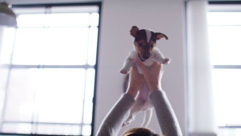 4K Young woman lifts her puppy and rests him on her chest as she strokes and plays with him, in slow motion