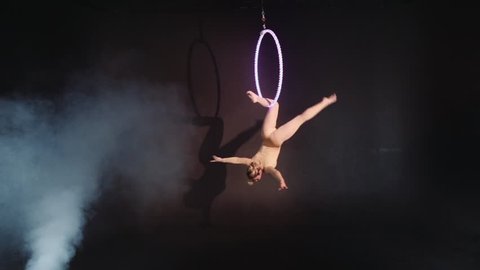 Blonde gymnast on aerial ring under a dome. Lovely tightrope walker in a trendy costume on a hoop in the circus. The concept of confidence and balance. Copy space text.