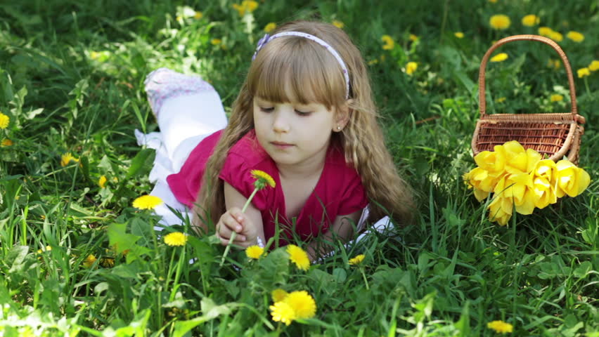 Girl in the meadow of dandelions. She is sniffing dandelions and looking at