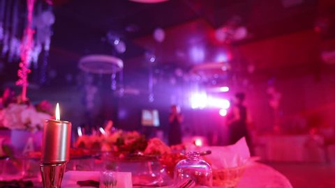 Candle on a table with a meal in the restaurant on the background of the illuminated scene, people silhouettes in the center of the restaurant hall, banquet hall, dark, shallow depth of field
