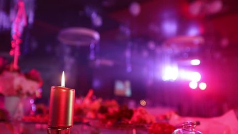 Candle on a table with a meal in the restaurant on the background of the illuminated scene. People silhouetted in the center of the restaurant hall, banquet hall, dark, shallow depth of field