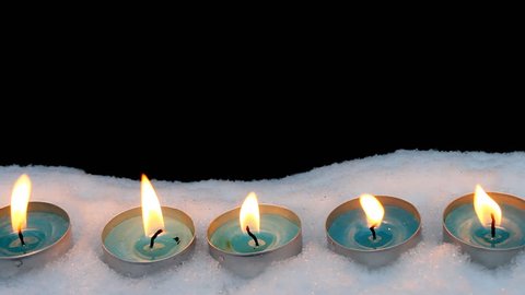 Candles burn in the snow on a black background