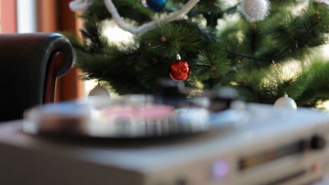 Close up: Vintage gramophone play back vinyl plate. Background: Live green Christmas tree with toys and lights. Jingle Bells.