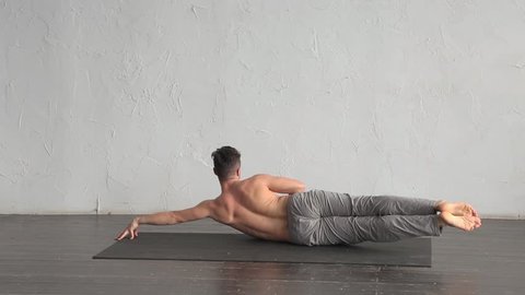 A young strong man doing yoga exercises. Studio shot over white wall background and black floor.