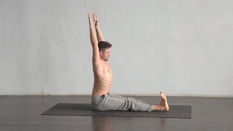 A young strong man doing yoga exercises. Studio shot over white wall background and black floor.