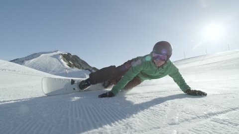 SLOW MOTION CLOSE UP: Snowboarder carving on perfectly groomed snow in mountain ski resort