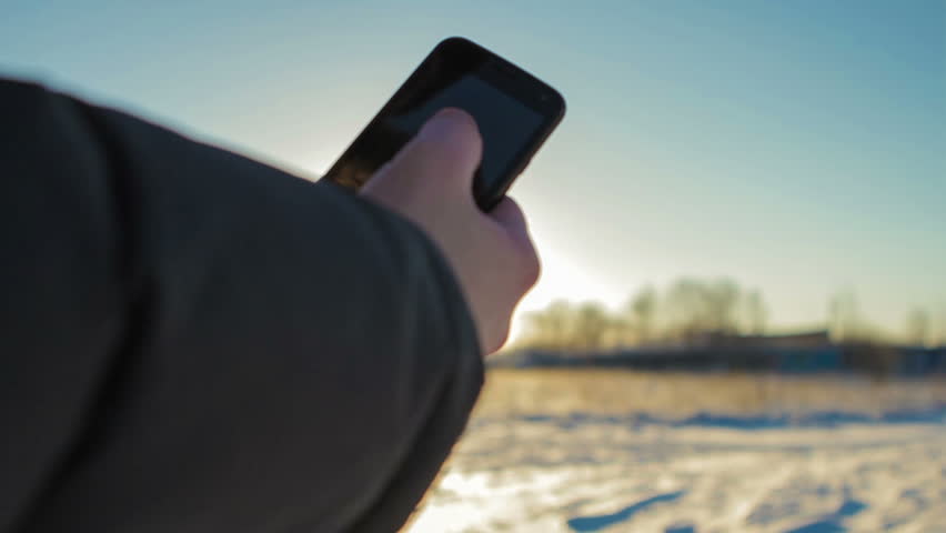 Man Uses the Phone in the Cold in the Open Field. he Drives a Finger Across the Screen.