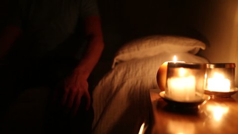 Person by the night stand relaxing before going to bed. Candlelights burn by the bed side. Man sitting by the bed side with candles burning