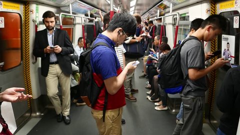 HONG KONG - MARCH 31, 2015: Young man stand in metro carriage, look to smart phone listen headphones. Mass Transit Railway in HK, train travelling through island line station, flickering outside
