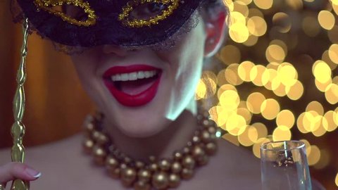 Beautiful sexy woman wearing venetian masquerade mask at party drinking champagne over holiday glowing background. Holiday make up, red lips, closeup. Full HD 1920x1080p slow motion video 