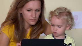 Serious face woman teaching baby girl using tablet computer. Closeup