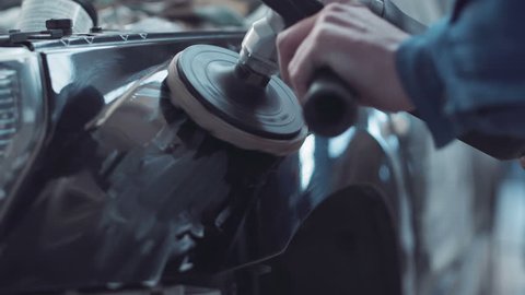 Mechanic using a rotary polisher on a the paintwork of a black car in a body shop to finish off a repair after an accident