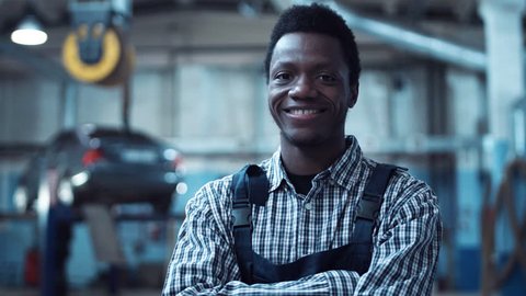 Auto mechanic wearing striped shirt smiles at camera as he stands with arms crossed