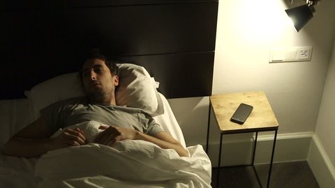 Man turns on the light suffering from insomnia. Person trying to sleep while thinking about life