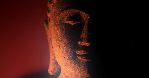 Calm and peaceful face of Buddha statue illuminated by candle light in darkness 