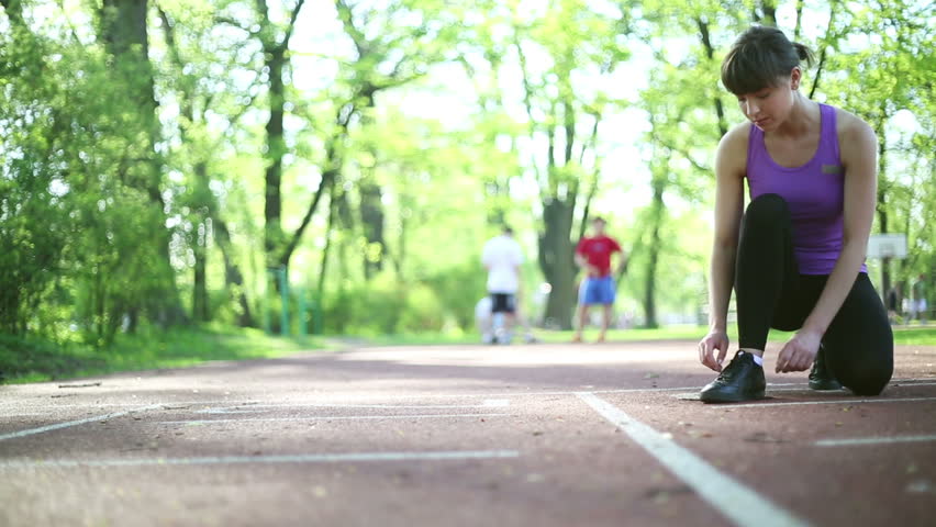 Young woman tying running shoes before run, dolly shot
