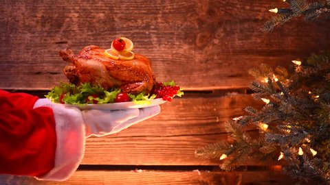 Christmas Holiday dinner. Santa Claus hand holding roasted Chicken, turkey or duck. Christmas and New Year food concept, over rural wooden background. Full HD 1080p video footage
