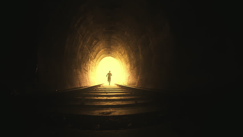 Silhouette of man running toward camera inside dark railway tunnel slow motion