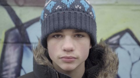 Close-up of a good-looking teenage boy wearing a hat and parka on a cold winter day. He is in an alley in the city during the daytime. 4K UHD.
