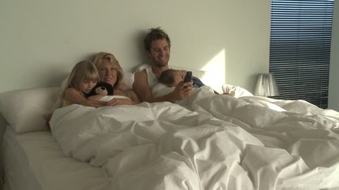 LONG SHOT PAN OF A FAMILY WATCHING TV IN BED