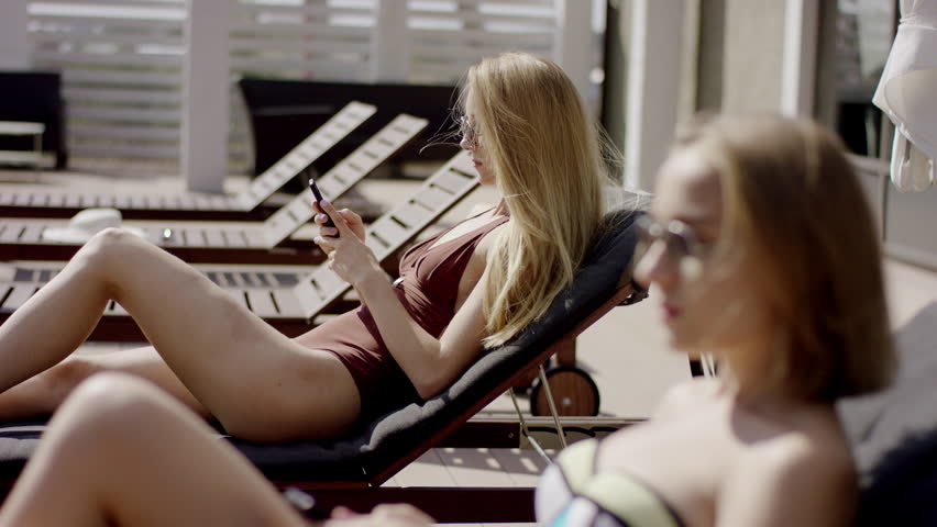 Young beautiful girls Relaxing with Phones in Deck Chair outdoor