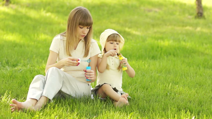 Mother and daughter sitting on the grass and blow bubbles
