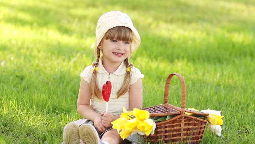 Girl licking a lollipop and sitting on the grass