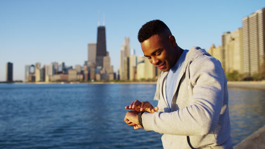 Ethnic African American male stretching and resting for heart health outdoors by Chicago skyscrapers wearing sportswear RED DRAGON