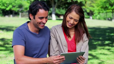 Happy couple looking at a tablet computer in a parkland