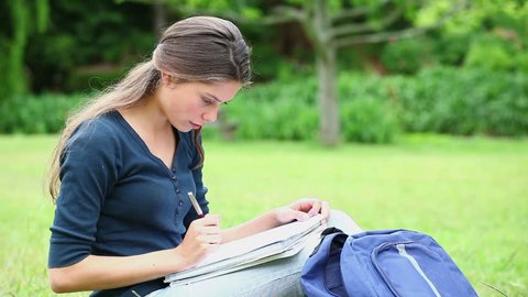 Cheerful student doing her homework in a park