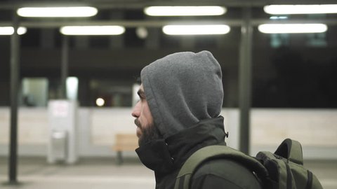 MIllenial youth in hoodie at the train station at night, slomo 100p.A hooded young man is waiting for the train or walking along the platform with or witout his hoodie on, at night.