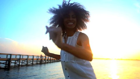 Portrait of young attractive African American female enjoying leisure and dancing on the beach at sunset