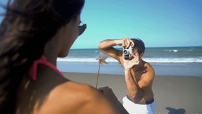Caucasian American male taking a photo of attractive Hispanic female wearing bikini on their beach holiday