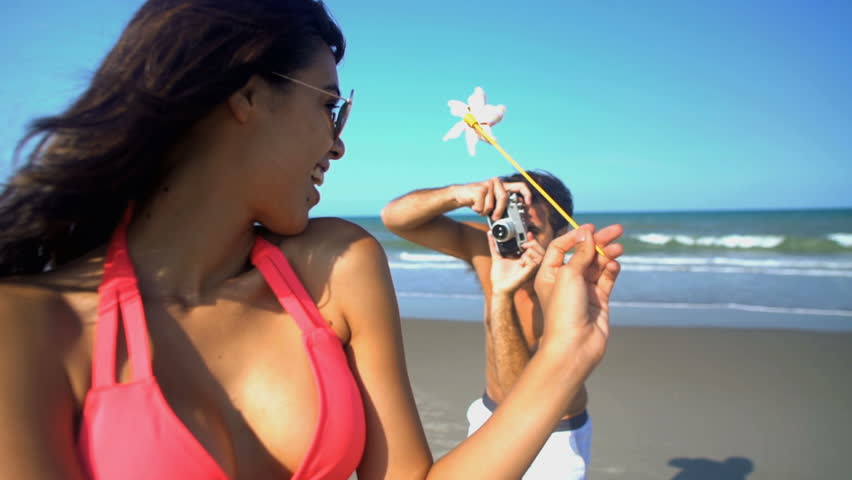 Young Caucasian man taking a picture of Latin American woman in bikini on their beach vacation