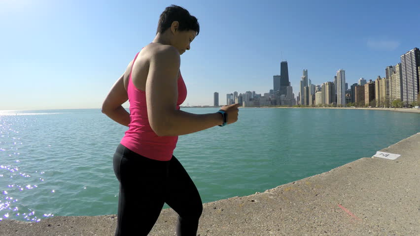 Profile of slim Ethnic African American female running in Chicago city by shoreline with smart watch