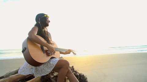 Cute Indian American girl wearing Retro style dress playing the guitar and singing on the beach sun flare