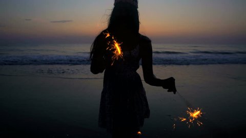 Silhouette of young beautiful Asian Indian woman celebrating birthday with sparklers on the beach at sunset