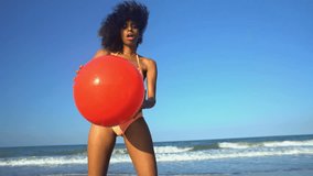 Portrait of young laughing ethnic girl with afro hair posing on her beach holiday with red ball