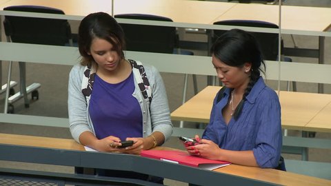 Female students on mobile phone texting in corridor