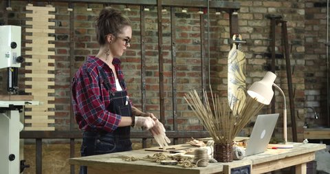 Hipster girl starts painting a wooden star in her lovely workshop. She’s dressed in checkered shirt. She has a brick wall behind her/Young Pretty Hipster Girl Engaged in Handmade