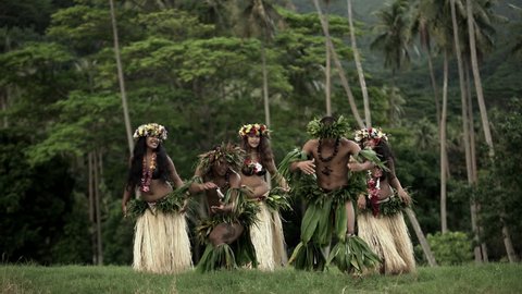 Barefoot Tahitian males in warrior dress with females in hula skirts and flower headdress performing a traditional dance at celebration ceremony South Pacific