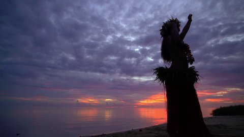 Polynesian girl in traditional grass skirt and flower headdress dancing on the beach at sunset hula style while entertaining barefoot outdoors Tahiti French Polynesia South, Pacific,