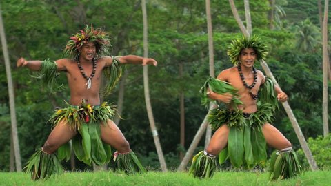Barefoot Tahitian male men in hula skirts and flower headdress performing a traditional warrior dance at celebration ceremony French Polynesia