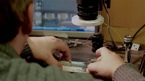 White man looks through handmade electronic microscope on repair of motherboard smartphone iphone