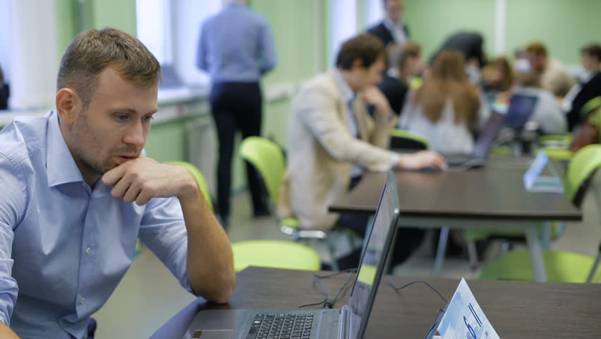 Two confident business people in discussing something while sitting at the desk in the classroom in fron of laptop.