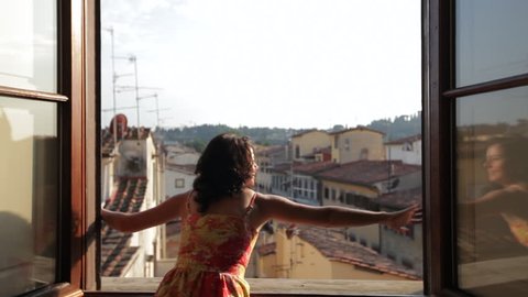 MH DS Woman Opening Windows Overlooking Old Town Rooftops / Florence, Italy