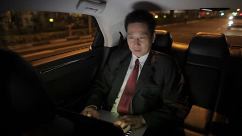 MH Businessman Riding in Back Seat of Car Working on Laptop at Night / Singapore