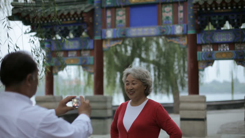 MS Mature man taking photo of elderly woman in front of traditional Chinese gate / Beijing, China