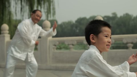 MS SELECTIVE FOCUS Young boy and mature man doing Tai Chi in a park by lake / Beijing, China