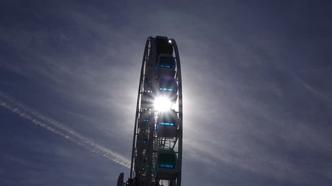 Bright sun light beam flash through Ferris wheel, slow rotating against dark sky. Low angle side view, sunshine flick over hanging cabins glass of modern observation SkyWheel construction